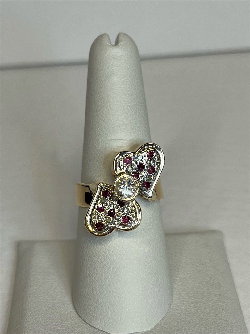 14k yellow gold double heart ring set with diamonds and rubies on a display finger